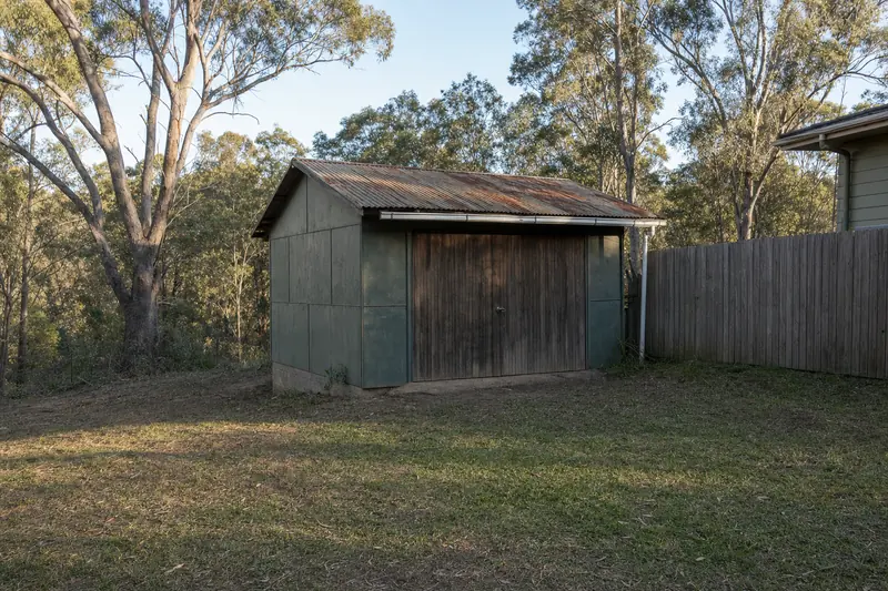 An old single garage clad in flat sheet panels with a rusting corrugated roof, in a backyard beside a timber fence — garage & shed demolition, Central Coast. Illustrative example.