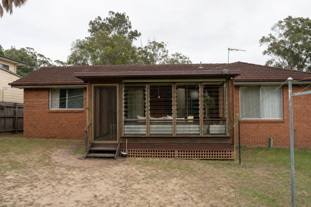 The back of a brick house with an old timber-framed sunroom fitted with glass louvres — partial demolition, Central Coast. Illustrative example.