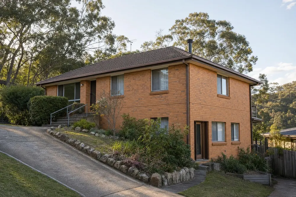 A brick house on a sloping block seen from below, standing two storeys at its low end and one at its entry — house demolition, Central Coast. Illustrative example.